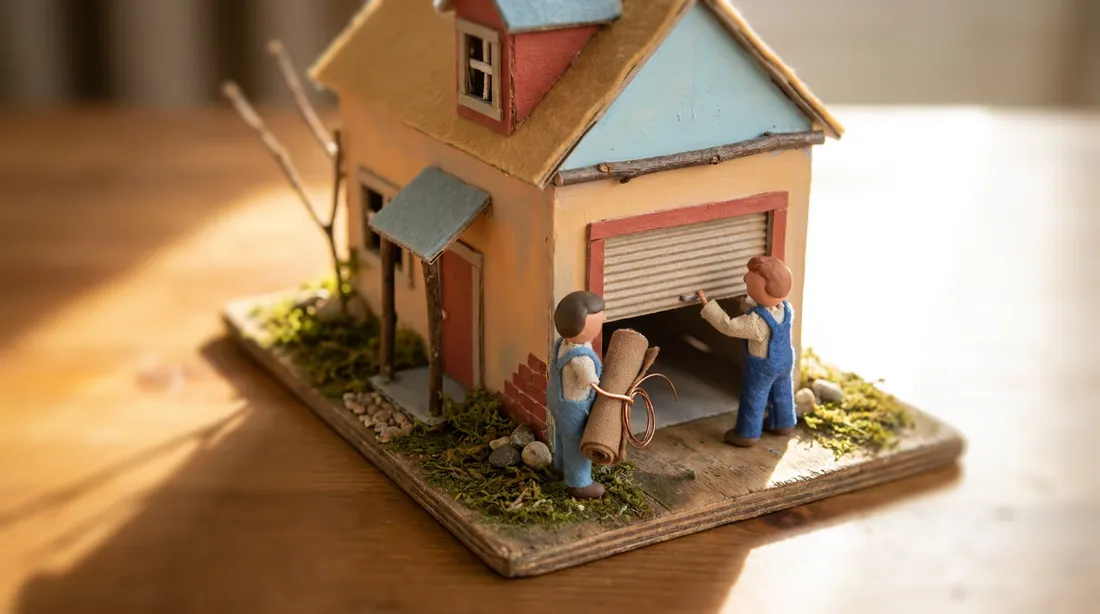 Miniature model set of installers fitting a roller garage door as light moves across the scene